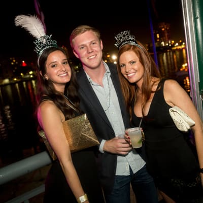 Three guests in Happy New Year tiaras on the waterfront deck at Pied Piper's New Year's Eve at Jackson's on Harbour Island, Tampa