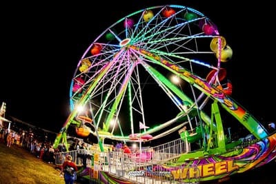 Neon-lit Ferris wheel towering over guests queuing on the lawn at night, Pied Piper's Haunted Carnival 2023