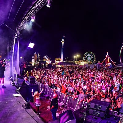 A packed crowd at the main stage of Pied Piper's Haunted Carnival 2025, with a Ferris wheel and rides lit up behind, Armature Works, Tampa