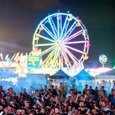 Rainbow-lit Ferris wheel towers over a packed crowd at night during XOXO Carnival with DJ Snake, May 2022