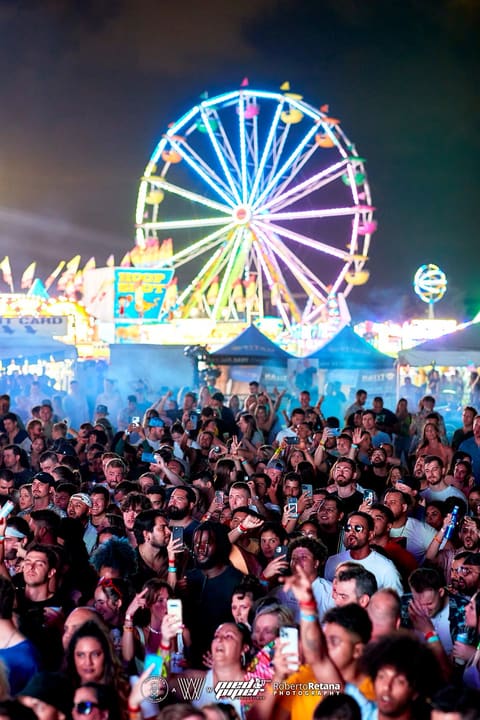 Rainbow-lit Ferris wheel towers over a packed crowd at night during XOXO Carnival with DJ Snake, May 2022